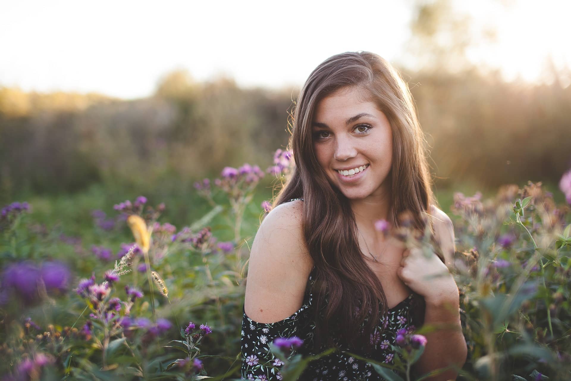 A girl smiles in a meadow of flowers.