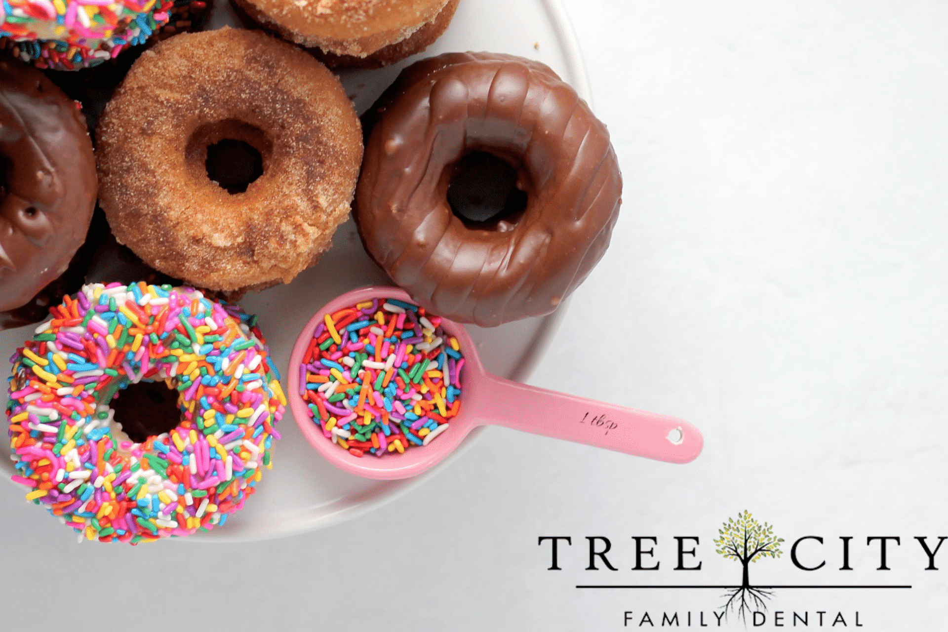 A plate of doughnuts and a tablespoon full of sprinkles.
